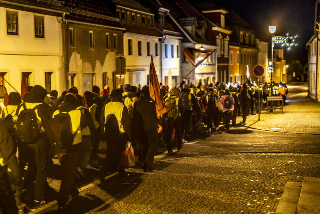 Eine große Gruppe von demonstrierenden läuft mit Fahnen und Warnwesten durch eine städtische Straße bei Nacht