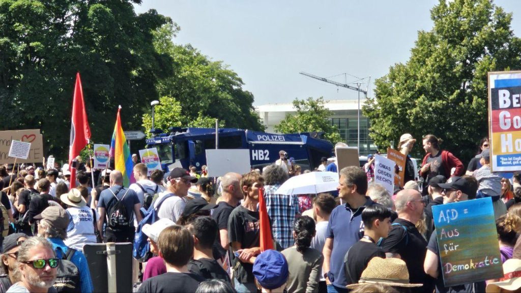 Eine Gruppe Menschen auf deiner Demo, bei Sonnenschein. Im Hintergrund ein Wasserwerfer der Bremer Polizei. Vereinzelt sind Demo-Schilder lesbar wie "AfD = Aus für Demokratie" oder "Omas gegen Rechts"